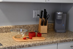 A kitchen counter with a glass bowl, red measuring cups, a wooden cutting board, a knife block, and a coffee maker. - A Relaxing Getaway on Grant in Geneva. (Geneva)