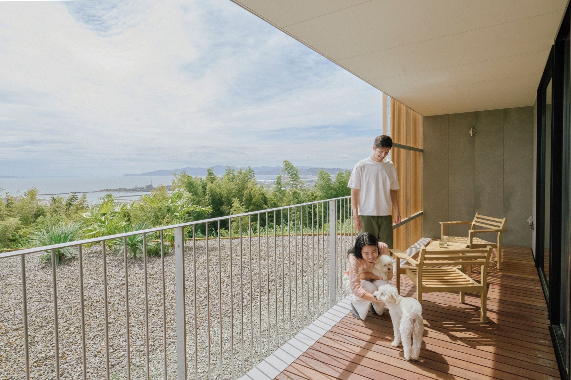 Een balkon met uitzicht op zee, een houten terras en een zithoek met stoelen.