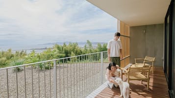 Een balkon met uitzicht op zee, een houten terras en een zithoek met stoelen.