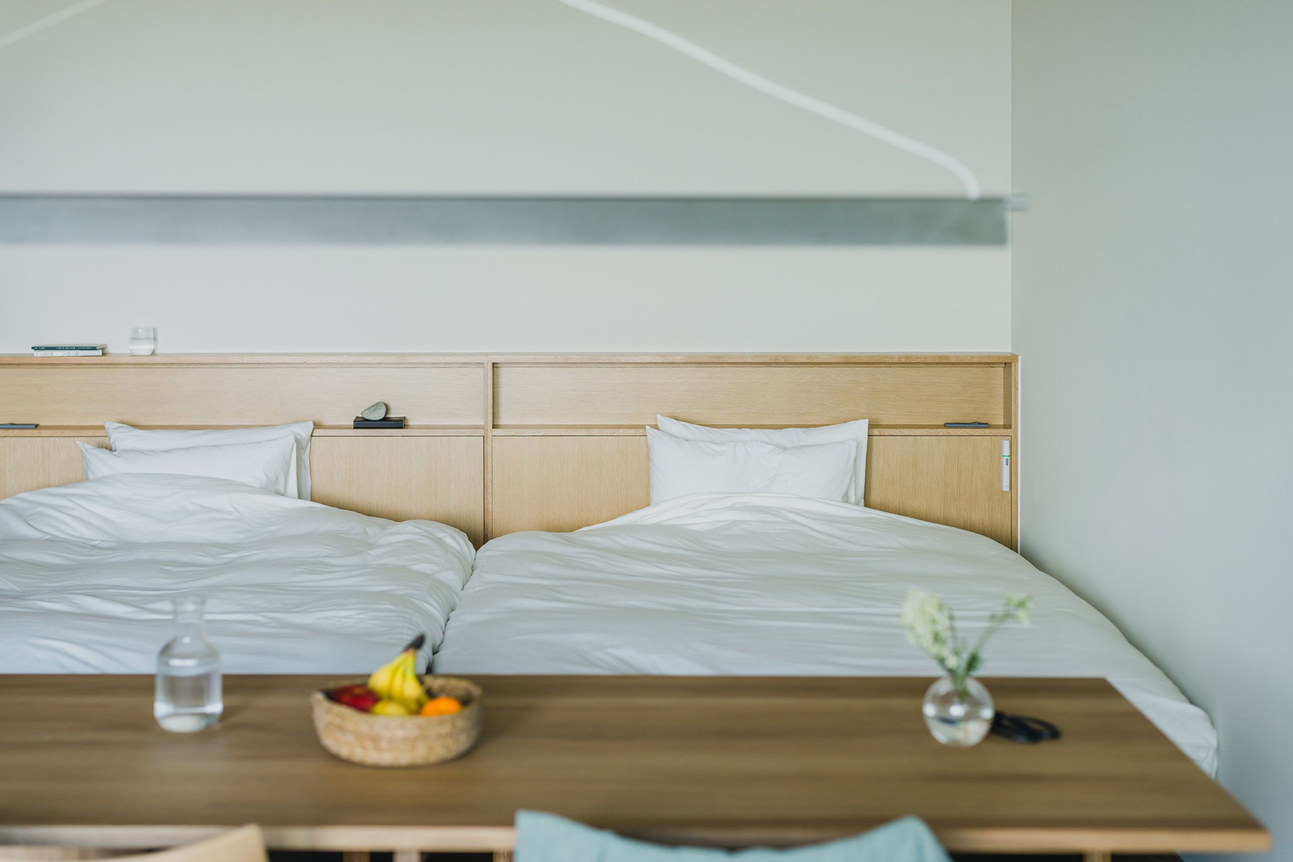 A hotel room with two beds, a wooden nightstand, a bowl of fruit, a vase with flowers, and a bottle of water.