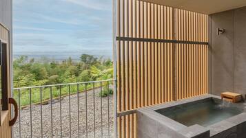 A modern bathroom with a built-in hot tub, a balcony with a view of the landscape, and a wooden privacy screen.
