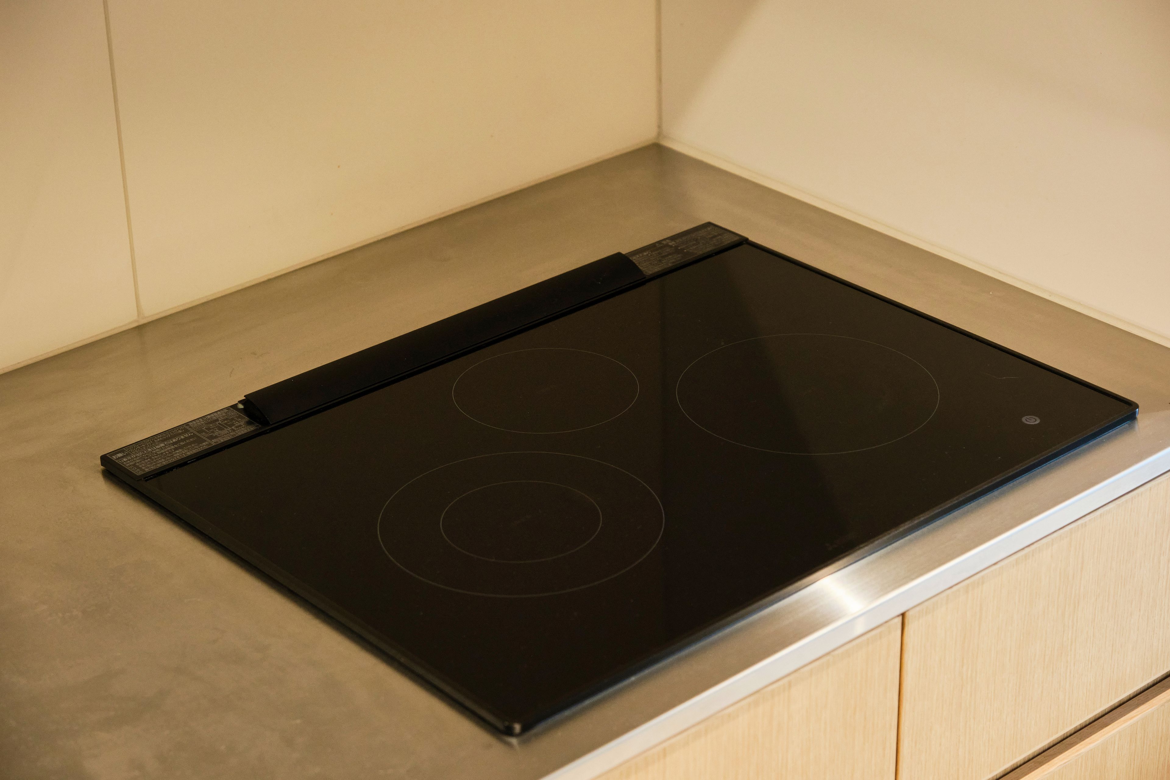 A black induction cooktop with four burners, located in a kitchen with light-colored cabinetry.