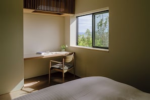 A bedroom with a bed, a desk with a chair, a window with a view of greenery, and a ceiling vent.
