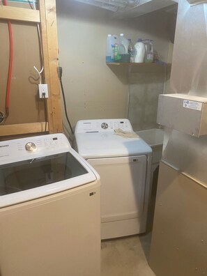 A laundry room with two washing machines, a shelf with cleaning supplies, and a refrigerator.
