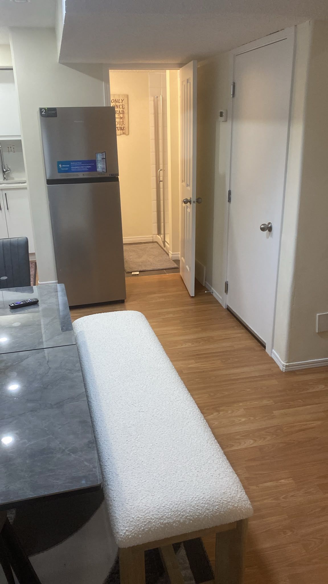 Une cuisine équipée d’un réfrigérateur, d’un banc et d’une porte donnant sur un couloir.