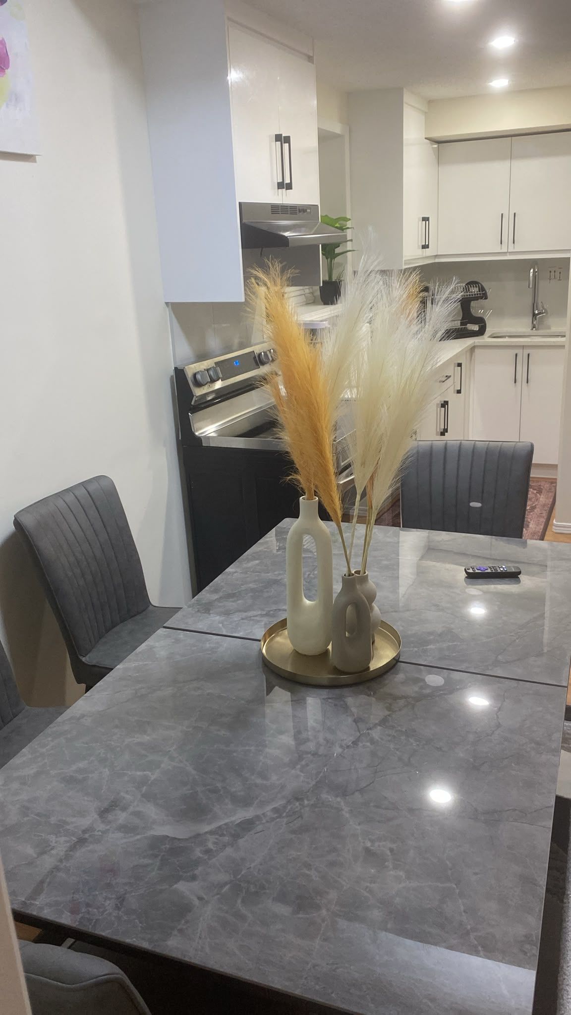 Un espace repas moderne avec une table en marbre, deux chaises et un vase contenant des plantes séchées.