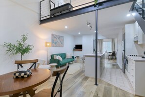A modern apartment with a dining area, a green sofa, a kitchen, and a staircase. - Manhattan Loft Central Location with Gym and Sauna (Brisbane)