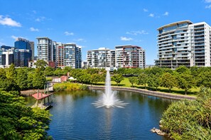 A cityscape with modern high-rise buildings, a central water body with a fountain, and surrounding greenery. - Manhattan Loft Central Location with Gym and Sauna (Brisbane)