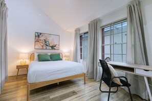 A bedroom with a bed, a desk, a chair, a window with curtains, and a painting on the wall. - Manhattan Loft Central Location with Gym and Sauna (Brisbane)