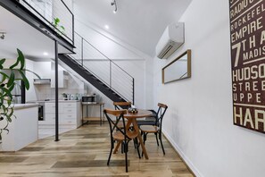 A modern kitchen with white cabinetry, a dining area with wooden chairs, and a staircase leading to an upper level. - Manhattan Loft Central Location with Gym and Sauna (Brisbane)