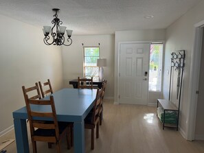 A dining area with a blue table and wooden chairs, a chandelier, a door, and a coat rack. - Recipe House by the Bay is a peaceful retreat in West Bradenton. (Bradenton)