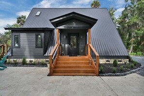 A modern two-story house with a dark grey exterior, a wooden front porch, and a stone foundation. - Peaceful Riverfront Retreat, Relax, Unwind & Enjoy the Water (Welaka)