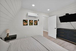 Un dormitorio con cama, cómoda, televisor montado en la pared y aire acondicionado.