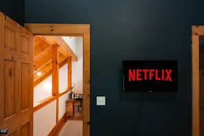 A room with a wooden ceiling, a wall-mounted TV displaying 'NETFLIX', and a door leading to another room. - Hot Tub Sauna Fire Pit 20 Min to Asheville (Fairview)