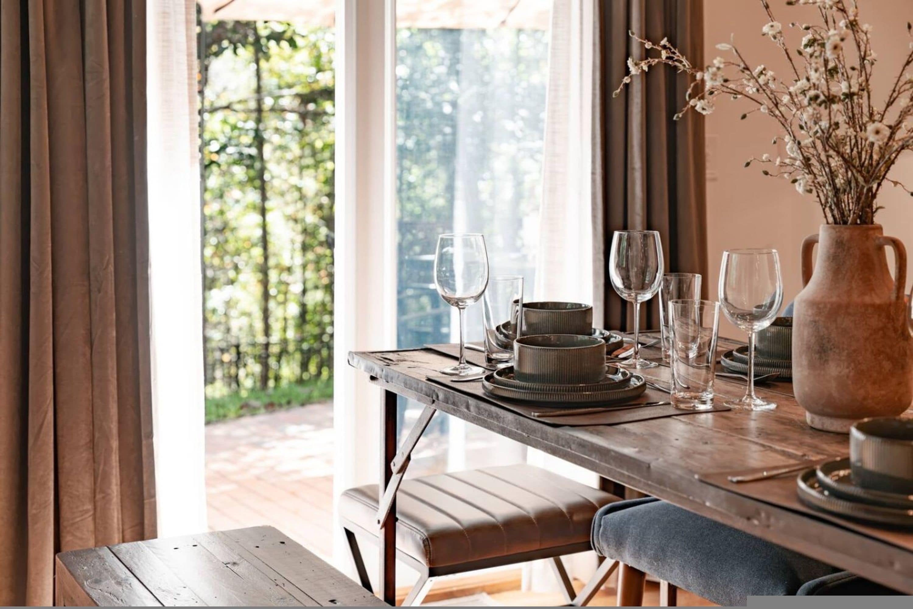 A dining table set with plates, glasses, and a vase with flowers.