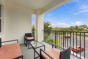 A balcony with a glass table and chairs, a view of a parking lot with cars, and a clear sky. - From Convention Days to Park Days 3BR Condo (Orlando)