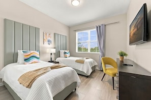 A hotel room with two beds, a desk, a chair, a window with curtains, and a flat-screen TV mounted on the wall. - From Convention Days to Park Days 3BR Condo (Orlando)