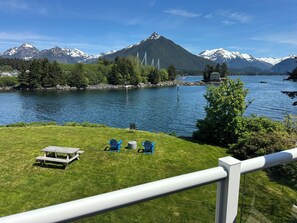 En vacker utsikt över sjön med en gräsyta, ett picknickbord, stolar och berg i bakgrunden.