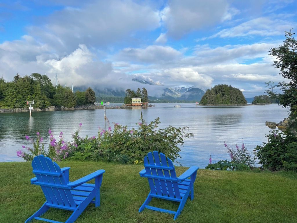 A lakeside view with two Adirondack chairs, a small building, and a distant island.