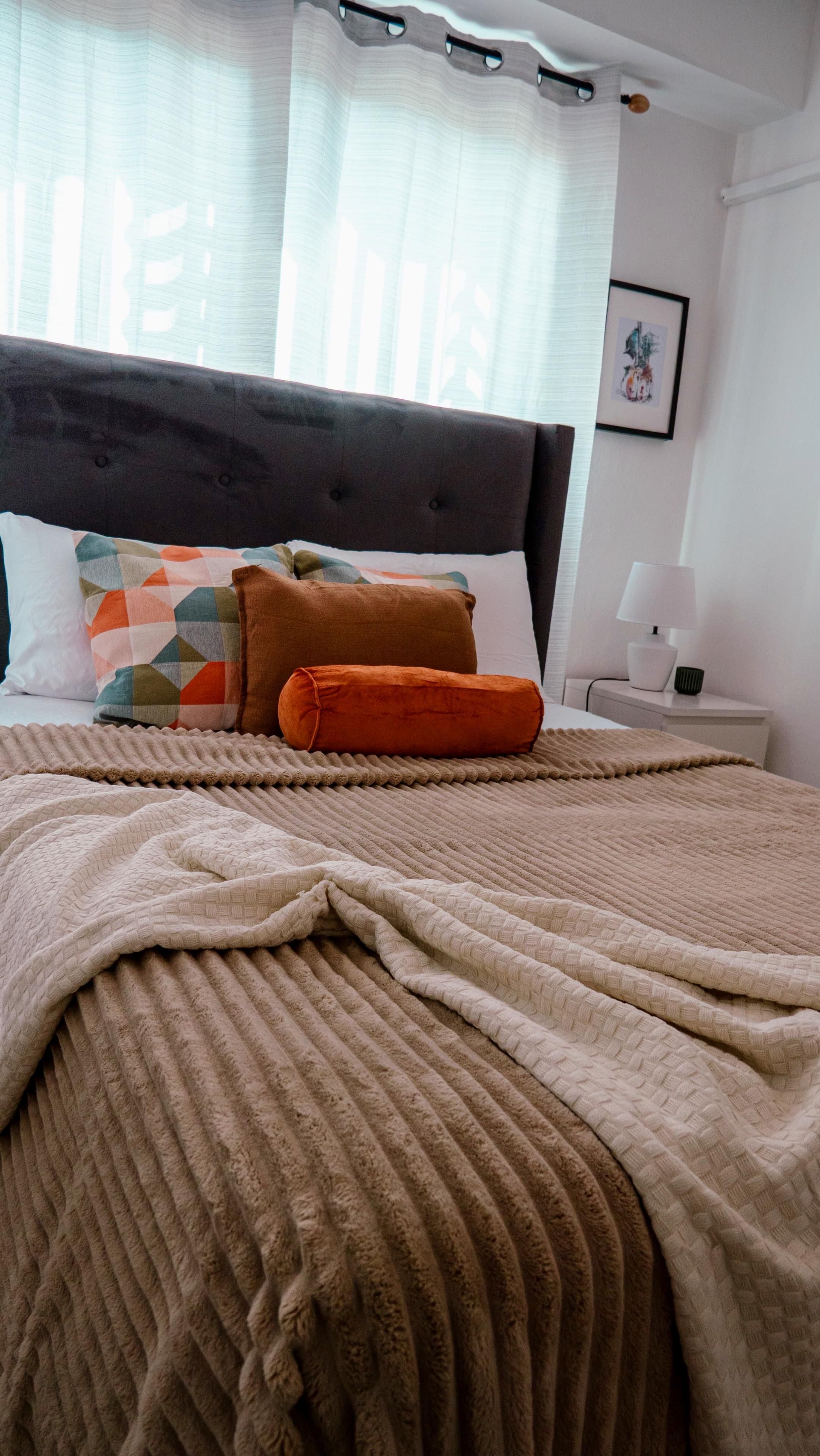 A neatly made bed with a brown blanket and pillows, a bedside table with a lamp, and a framed picture on the wall.