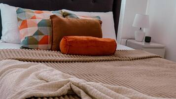 A neatly made bed with a brown blanket and pillows, a bedside table with a lamp, and a framed picture on the wall.