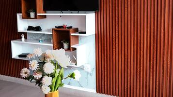 A modern living room with a flat-screen TV mounted on a wall, a wooden entertainment unit below, and a black coffee table with a vase of flowers.