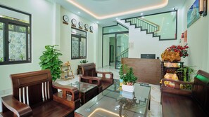 A modern hotel lobby with a glass-top dining table, wooden chairs, a staircase, and a reception desk. - Maison De Sonic - Hoi An Boutique Villa (Da Nang)