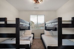Une chambre avec des lits superposés, une fenêtre avec des stores et un ventilateur de plafond.