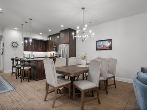 A modern kitchen with dark wood cabinets, a central island, and a dining area with a wooden table and upholstered chairs. - Red Rock Adventure Oasis with a Private Hot Tub, game room, and Fire Pit! (Santa Clara)