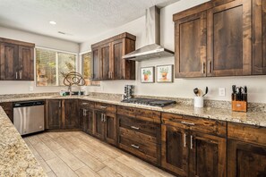 A kitchen with dark wooden cabinets, a stainless steel dishwasher, a granite countertop, and a stainless steel range hood. - Paradise Village 102, Private Spa, Pool table, Foosball, Ping Pong and More! (Santa Clara)
