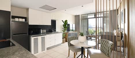 A modern kitchen with a built-in oven, a dining area with a round table and chairs, and a view of the city through large windows.