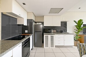 A modern kitchen with a built-in oven, a refrigerator, and a microwave. - Secure One Bed Apartment Modern and Spacious (Cape Town)