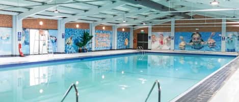Piscina interna com água cristalina, cercada por paredes com murais e teto alto com vigas aparentes.