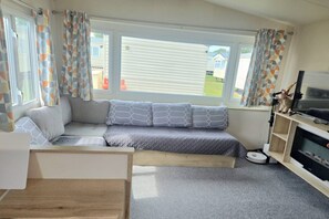 A modern living room with a sofa, a television, and a window with curtains. - Located at New Beach Holiday Park in Dymchurch (Romney Marsh)