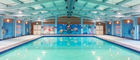 Piscina interna com teto alto e um mural na parede.