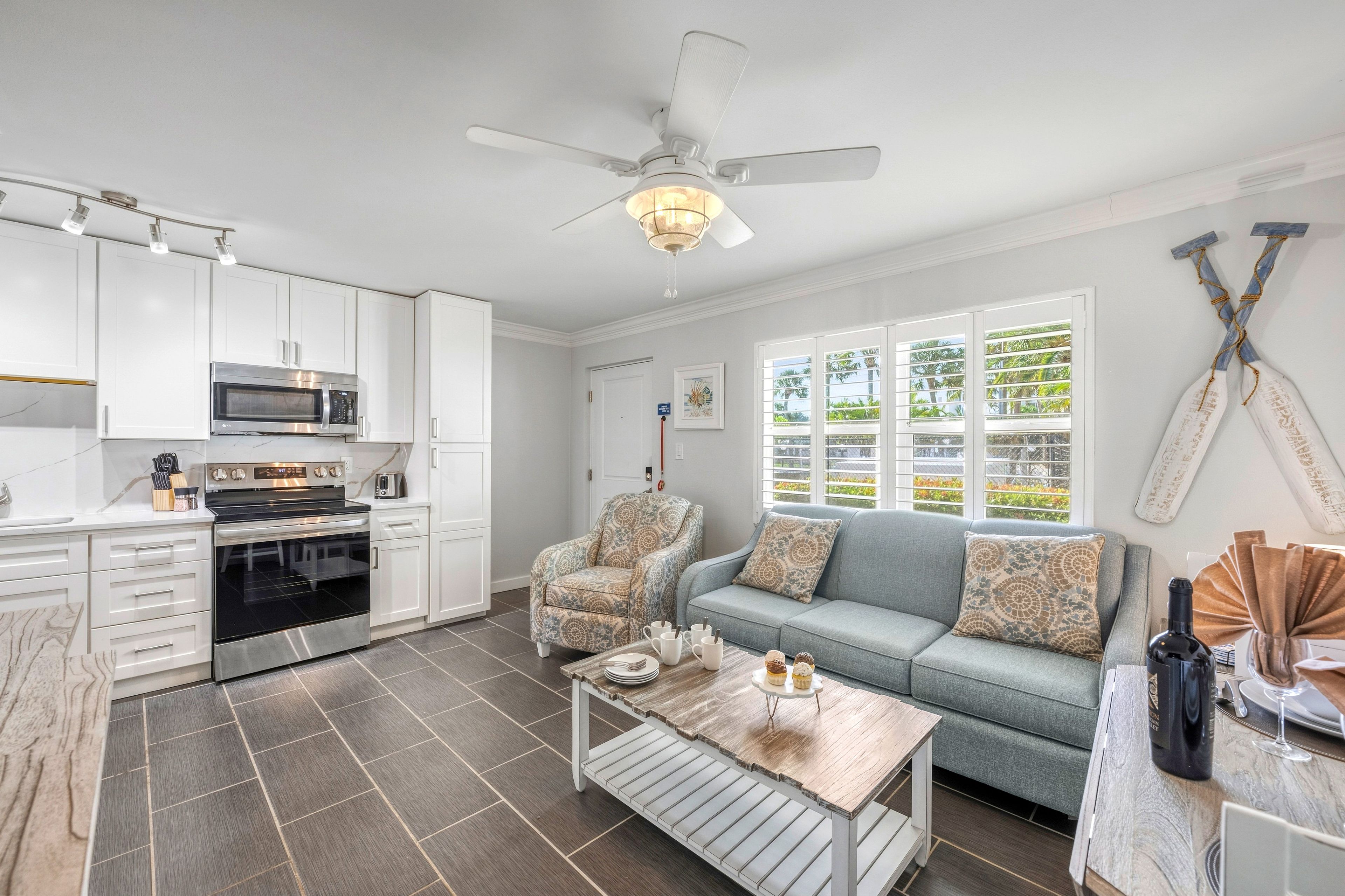 A modern kitchen with white cabinets, a microwave, oven, and a ceiling fan.