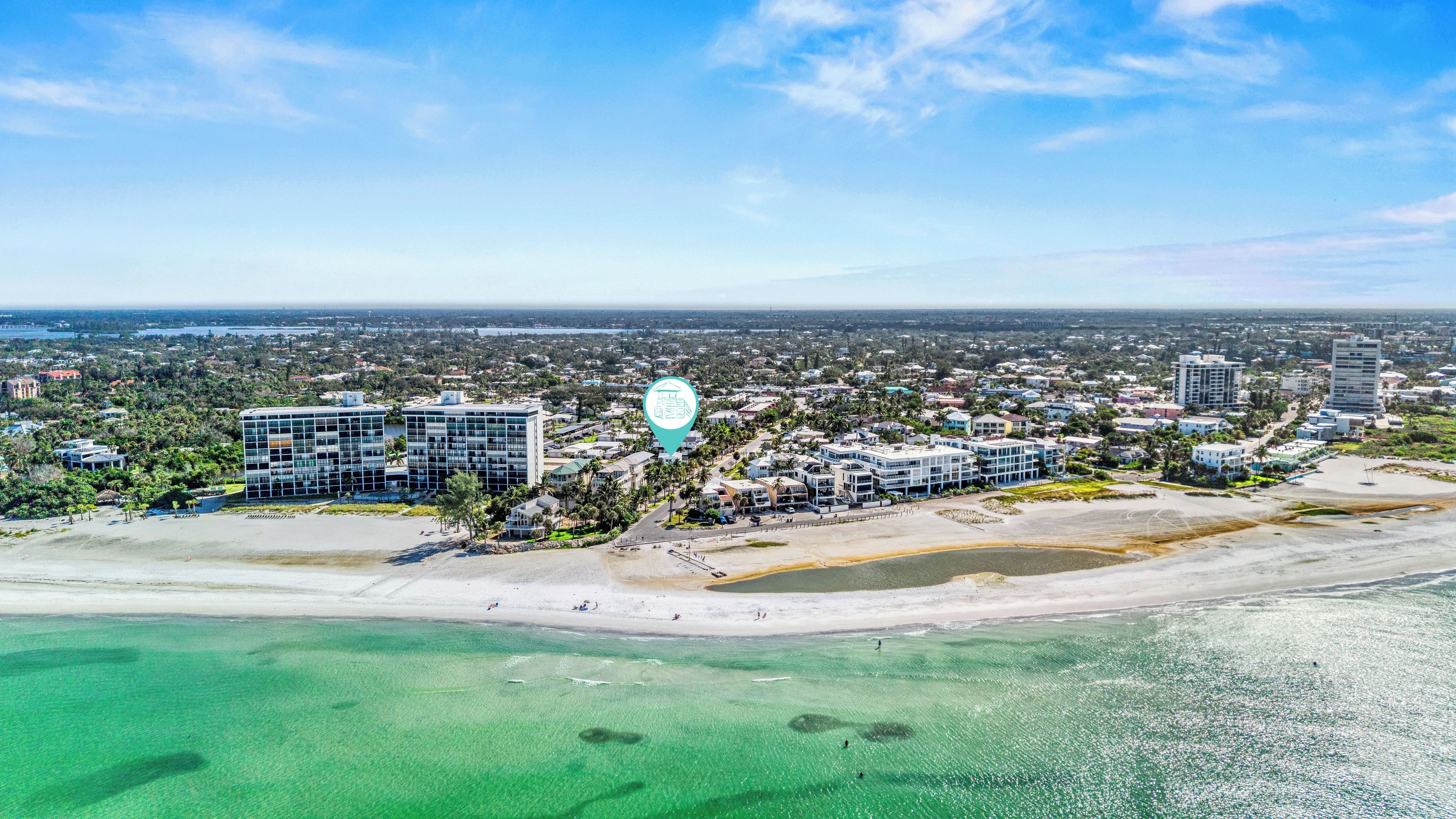 A coastal cityscape with modern buildings, a beach, and clear turquoise waters.
