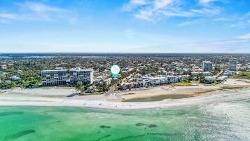 A coastal cityscape with modern buildings, a beach, and clear turquoise waters.