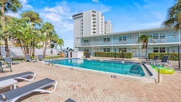 A swimming pool with lounge chairs and palm trees, surrounded by a fence.