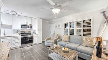A modern kitchen with built-in appliances, a dining area with a table and chairs, and a living room with a sofa and a ceiling fan.