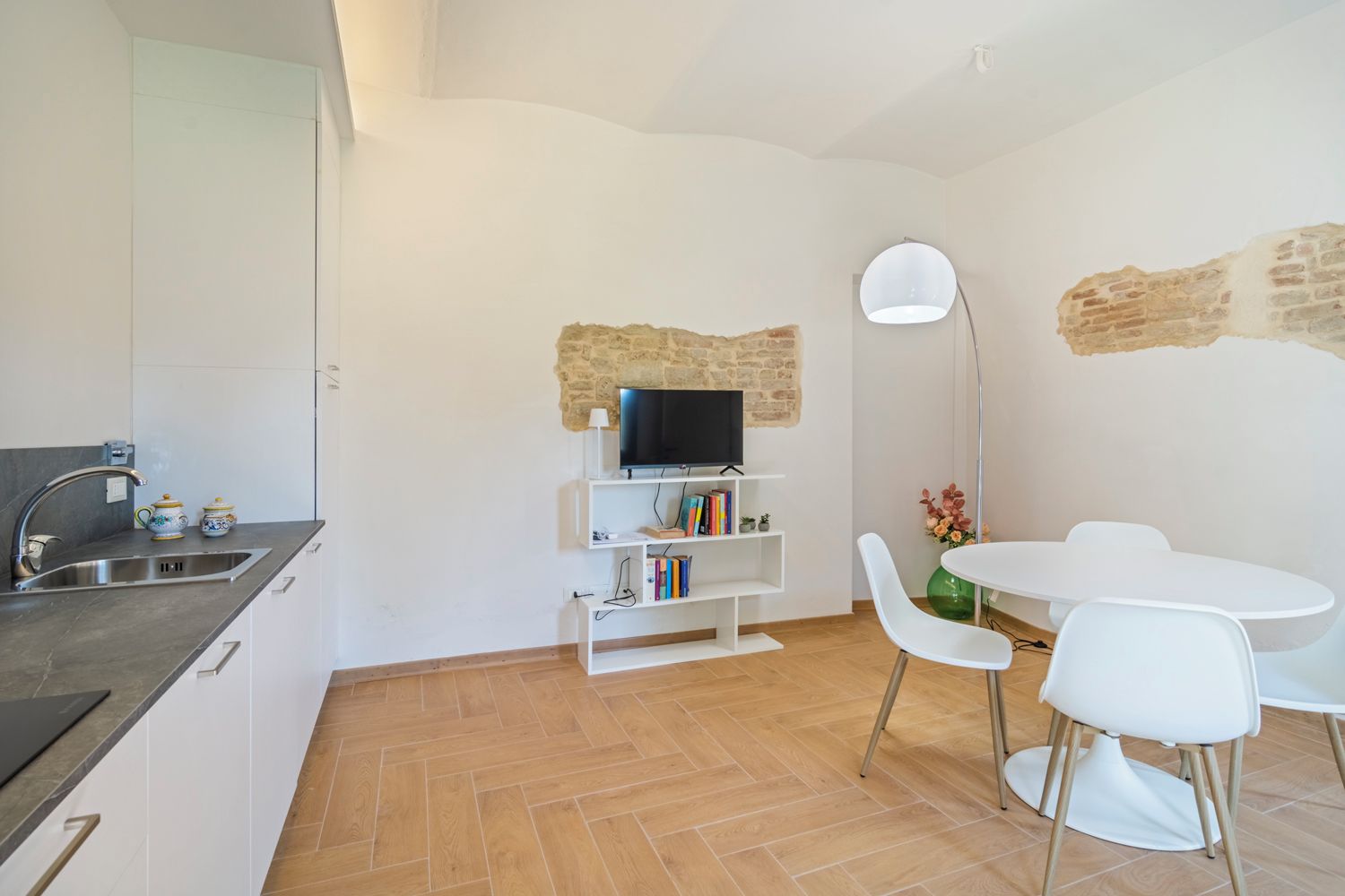 Une cuisine compacte dotée d’un téléviseur intégré, de meubles blancs et d’un coin repas avec une table ronde et des chaises.