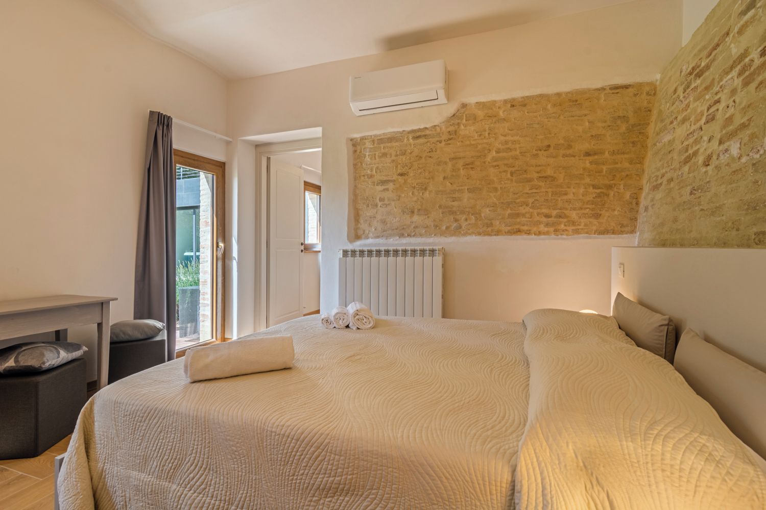 Une chambre d’hôtel avec un grand lit, un radiateur, une fenêtre avec des rideaux et un mur en briques.