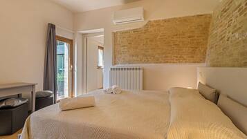 Une chambre d’hôtel avec un grand lit, un radiateur, une fenêtre avec des rideaux et un mur en briques.