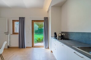 Cuina moderna amb vista a un jardí, zona de dinar amb una cadira, i una porta que dona a l'exterior.