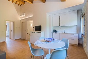 Eine kompakte Küche mit weißen Schränken, einem Esstisch mit blauen Stühlen und einem Fernseher auf einem Schrank.