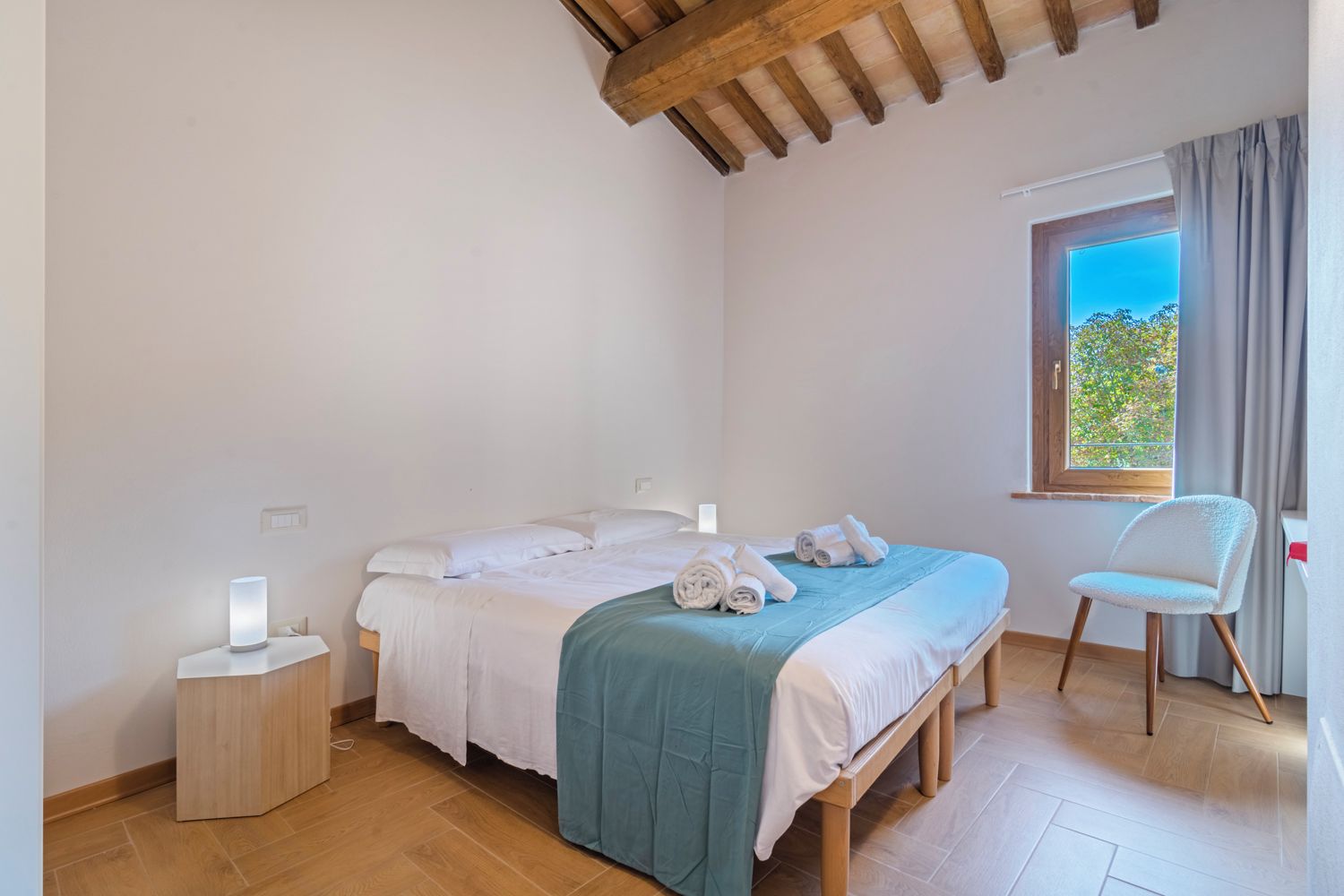 Ein Schlafzimmer mit einem Bett, einem Sessel, einem Nachttisch und einem Fenster.