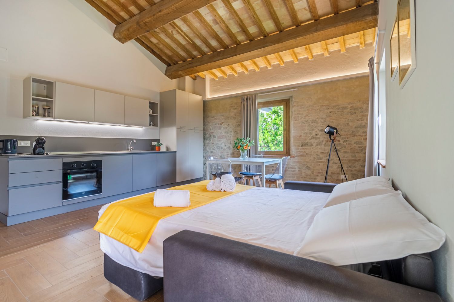 Ein modernes Schlafzimmer mit Bett, einer kleinen Küchenzeile, einem Esstisch und einer Steinwand.