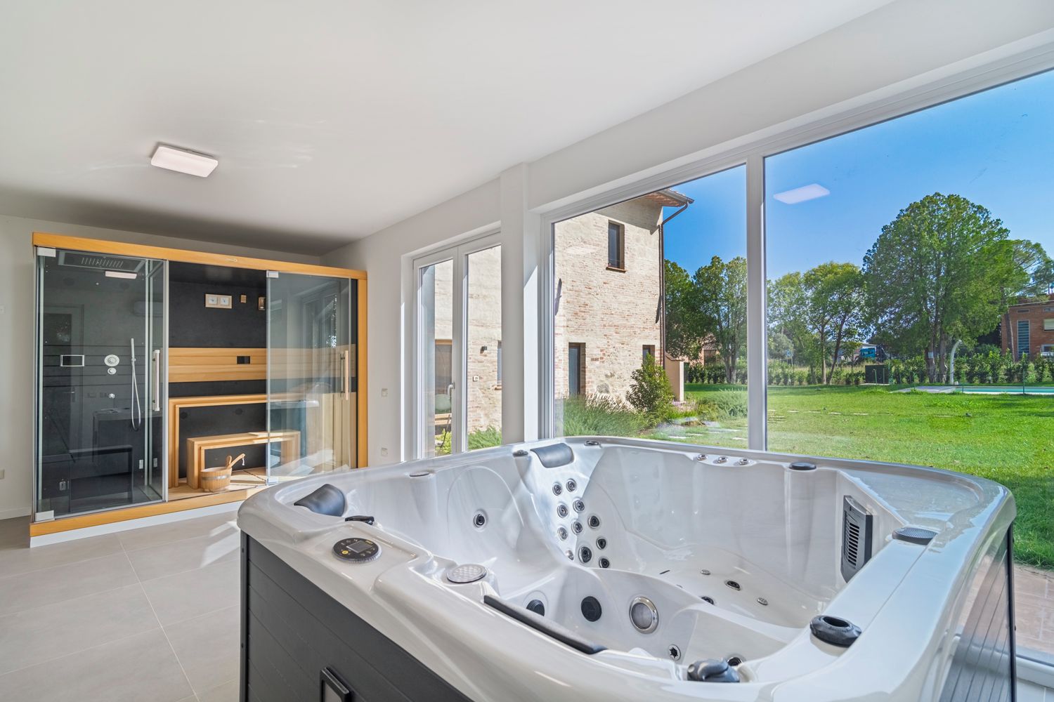 A modern bathroom with a large bathtub, glass shower enclosure, and a view of a brick building and greenery.