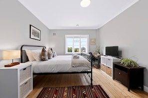 A bedroom with a bed, bedside table, lamp, TV, desk, chair, and a window with a view. - Serene 2 Bed 2 Bath Apt (London)