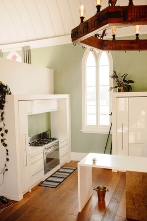 A compact kitchen with white cabinetry, a gas stove, and a window providing natural light. - The Church Accommodation
Reefton (Reefton)